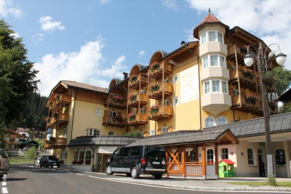 Žltá budova v alpskom štýle s drevenými balkónmi a niekoľkými zaparkovanými autami vpredu.