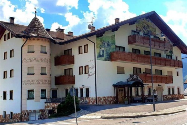 Budova hotela s drevenými balkónmi a maľbami na fasáde pod oblakmi.