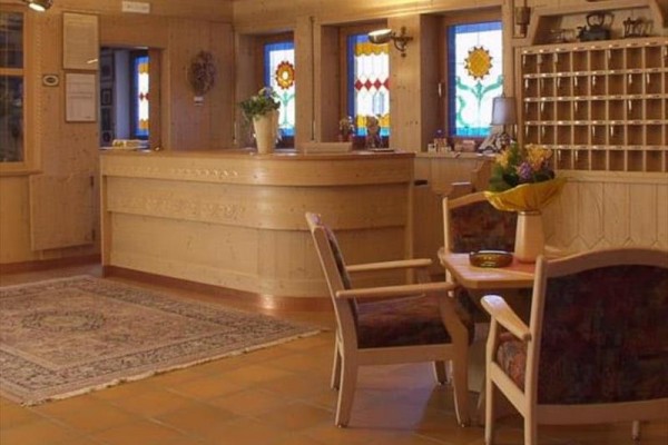 Hotelová recepcia s dreveným nábytkom a farebnými vitrážovými oknami.