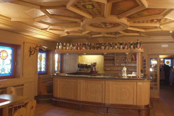 Drevený interiér kaviarne s barom, fľašami alkoholu a vitrážovými oknami.  