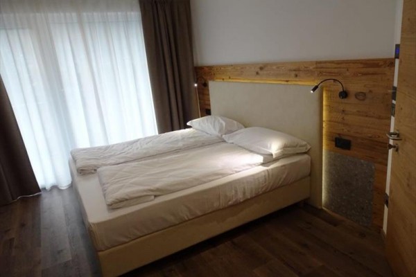 Manželská posteľ v modernej spálni s drevenými prvkami a závesmi.