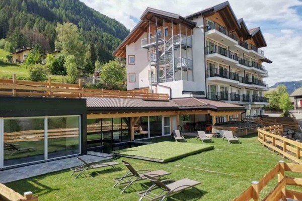 Horský hotel s terasou a ležadlami na zelenom trávniku.