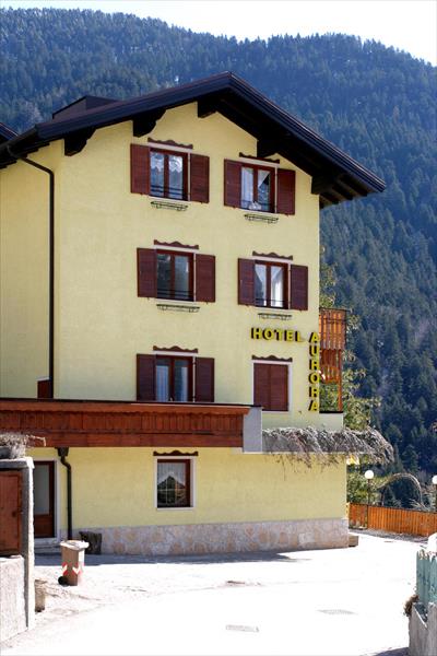 Žltý hotel s hnedými okenicami pred zalesneným kopcom.  