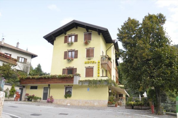 Trojposchodový žltý hotel s drevenými okenicami a kvetmi na balkónoch pri ceste.
