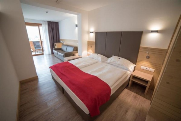Moderná hotelová izba s manželskou posteľou, červenou prikrývkou a balkónom.
