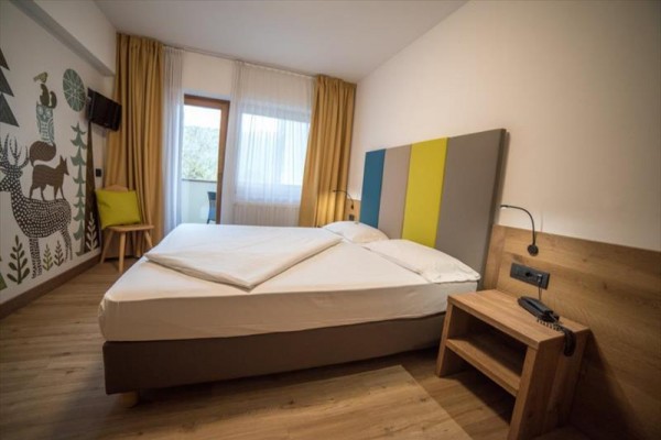 Moderná hotelová izba s manželskou posteľou, farebným čelom a nástennou maľbou zvierat.