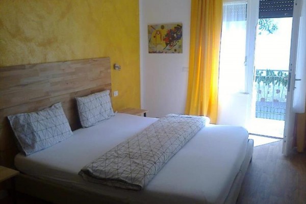 Svetlá spálňa s manželskou posteľou, žltými závesmi a balkónovými dverami.