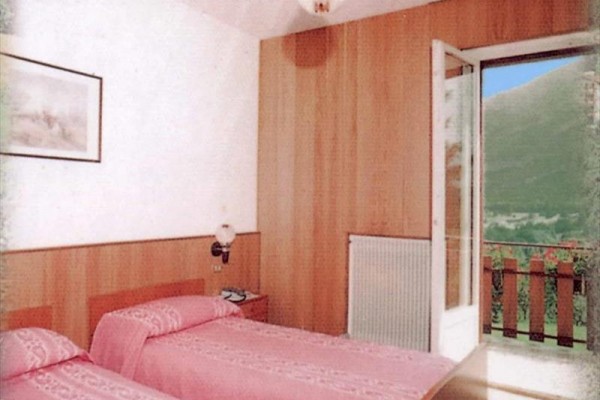Izba s dvoma posteľami s ružovou posteľnou bielizňou a otvorenými dverami na balkón.