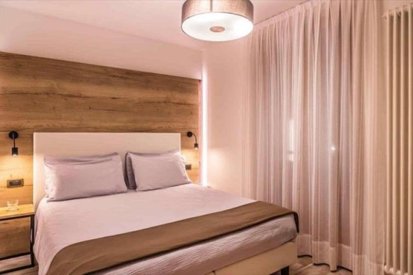 Moderne zariadená spálňa s drevenou stenou, manželskou posteľou a elegantným osvetlením.