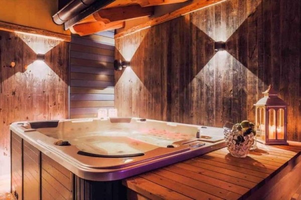 Vnútorná jacuzzi obklopená drevenými panelmi s osvetlením a lampášom na stole.