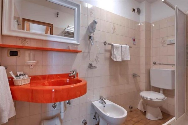 Kúpeľňa s oranžovým umývadlom, toaletou a bidetom.