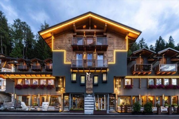 Moderný horský hotel s dreveným obložením a osvetlením, obklopený lesom.