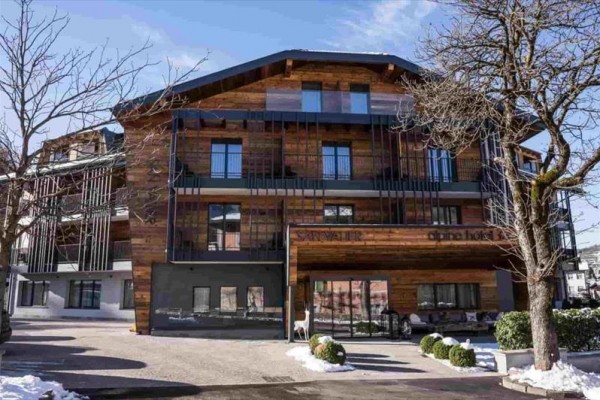 Moderný drevený hotel s balkónmi a stromami v popredí.