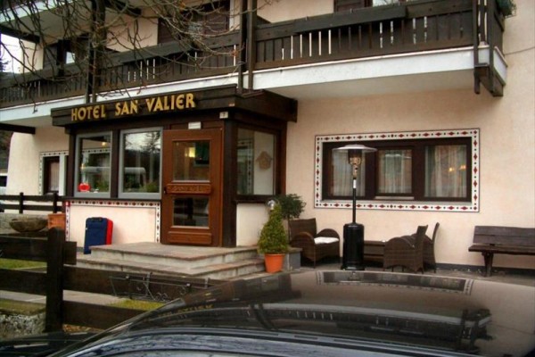 Vchod do hotela San Valier s lavičkami a kvetináčom pred ním.