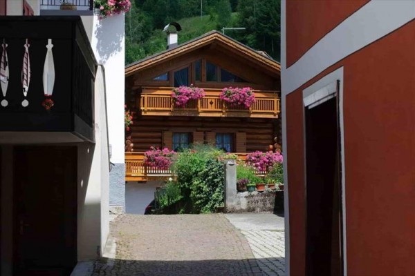 Drevený chalupový dom s kvetmi na balkónoch medzi dvoma budovami.