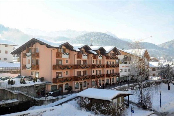 Zasnežený hotel s balkónmi a horami v pozadí.