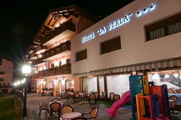 Nočný pohľad na osvetlený hotel s vonkajším posedením a detským ihriskom.