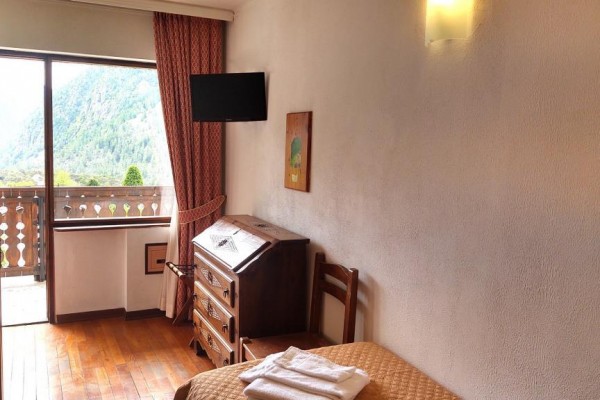 Jednolôžková izba s dreveným nábytkom a výhľadom na hory z balkóna.