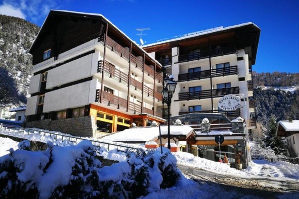 Zasnežený horský hotel s drevenými balkónmi počas slnečného dňa.