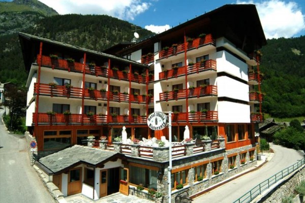 Veľký hotel s drevenými balkónmi medzi horami a lesom.