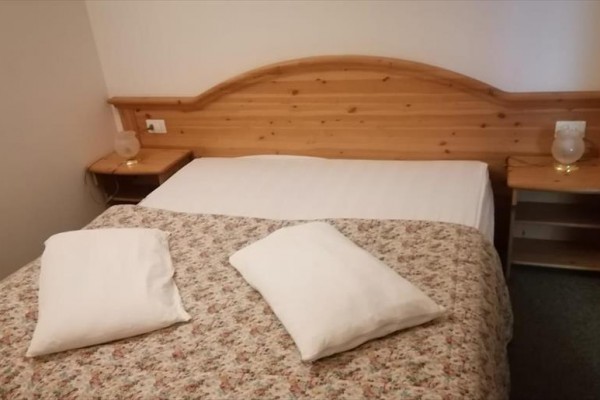 Manželská posteľ s dreveným čelom a kvetinovým prehozom.