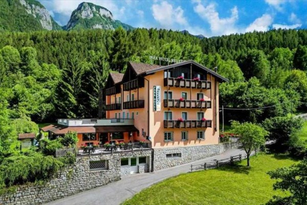 Hotel obklopený lesmi a horami s modrou oblohou v pozadí.
