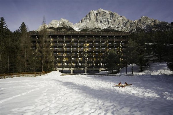 Veľký hotel obklopený snehom a horami v pozadí.