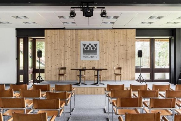 Konferenčná miestnosť s dreveným pódiom, dvoma stoličkami a logom 