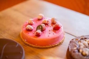 Guľatý ružový zákusok ozdobený malinami a cukrom.