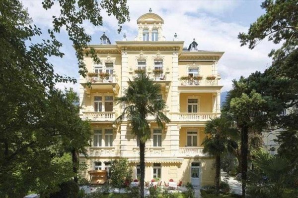 Historická žltá budova obklopená stromami a palmami.