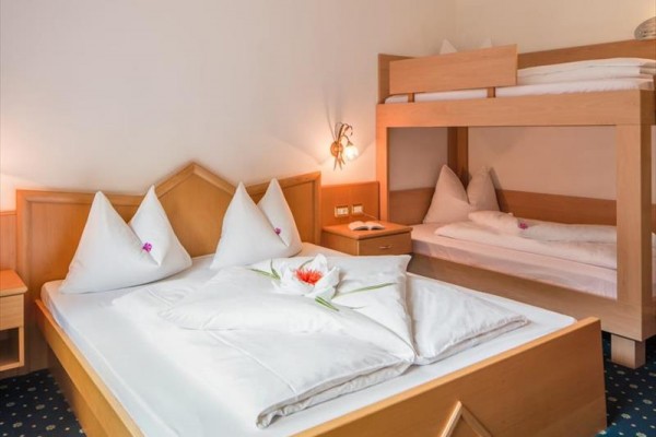 Hotelová izba s manželskou posteľou a poschodovou posteľou, posteľné prádlo zdobené kvetmi.