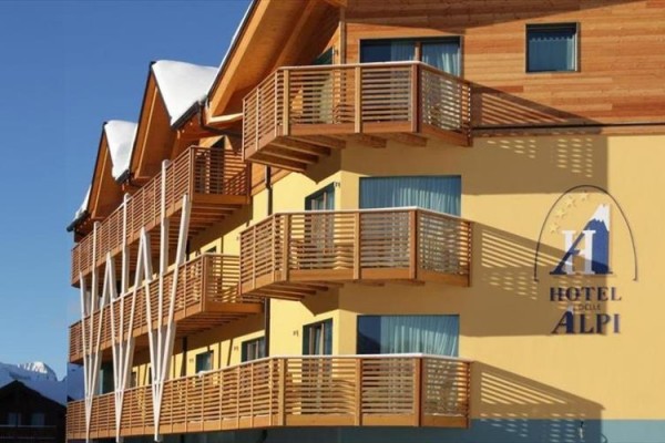 Hotel s drevenými balkónmi a logom na žltej fasáde.