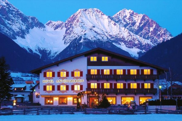 Horský hotel so svietiacimi oknami pred zasneženými vrcholmi hôr.