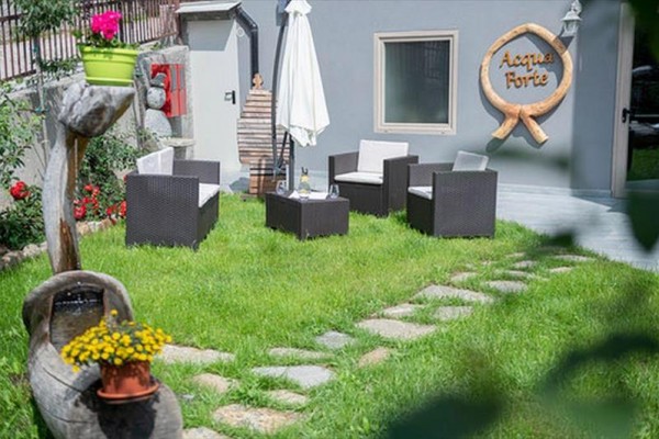 Záhrada s ratanovými stoličkami, stolom a slnečníkom pred šedou budovou s nápisom 