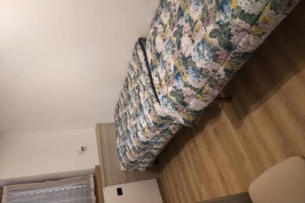 Jednolôžko s vzorovanou prikrývkou v izbe s drevenou podlahou.