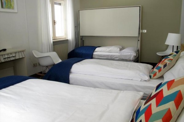 Tri postele v moderne zariadenej izbe s bielymi stenami a farebnými vankúšmi.