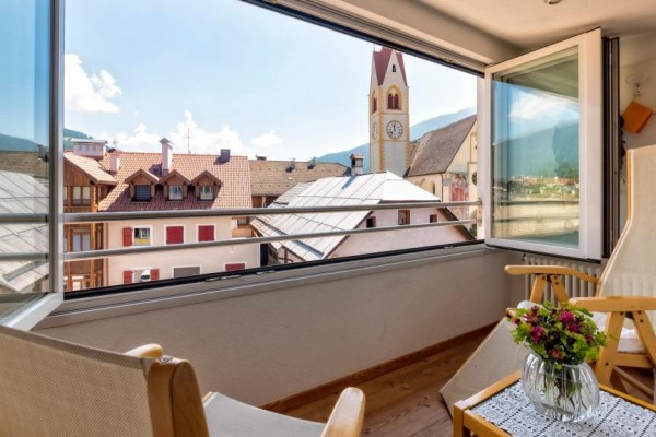 Výhľad z balkóna s drevenými kreslami na zvonicu kostola a horské panorama.