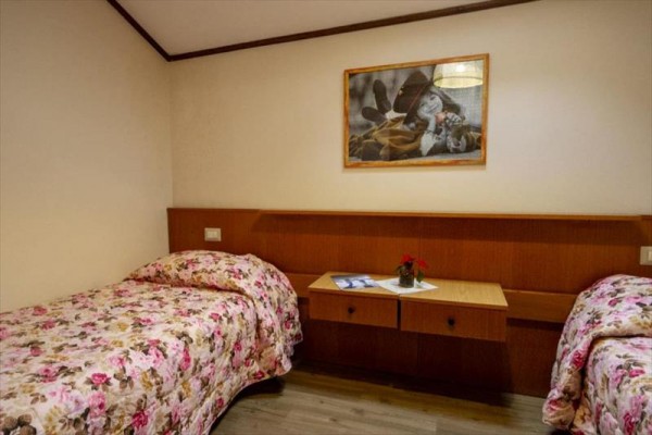 Izba s dvoma samostatnými posteľami s kvetinovými prikrývkami, nočným stolíkom a obrázkom na stene.