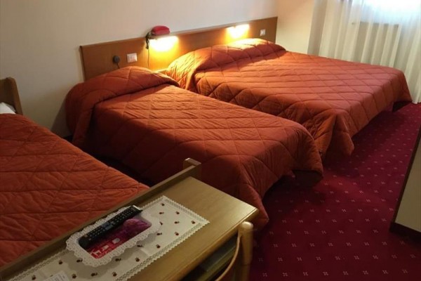 Tri postele s červenými prikrývkami v hotelovej izbe.