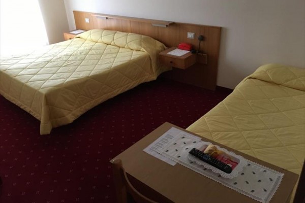 Dve jednolôžkové postele so žltými prehozmi v hotelovej izbe s červeným kobercom.