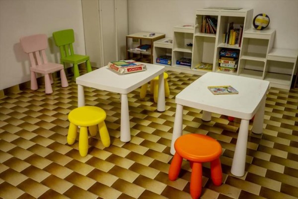 Detská herňa s farebnými stoličkami a stolmi na šachovnicovej podlahe.