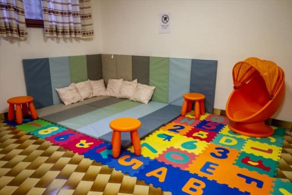 Detský kútik s vankúšmi, farebnými podložkami a oranžovými plastovými stoličkami.