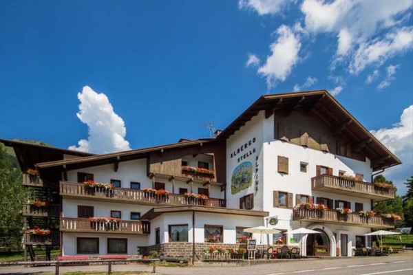 Hotel s drevenými balkónmi a kvetinovou výzdobou pod modrou oblohou.
