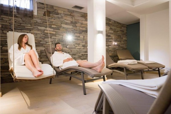 Dvaja ľudia relaxujú v županoch na lehátkach v miestnosti s kamennou stenou.