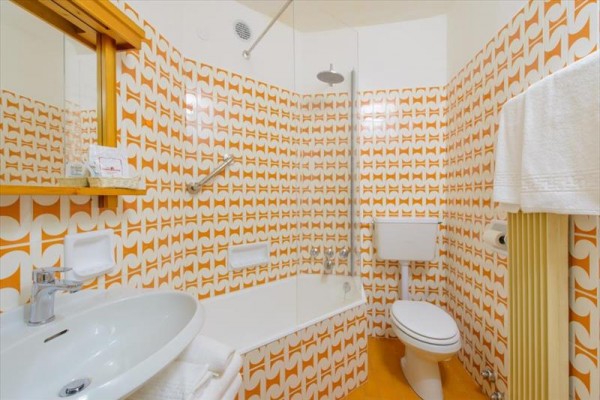 Kúpeľňa s retro oranžovými vzorovanými obkladačkami, vaňou a závesným záchodom.