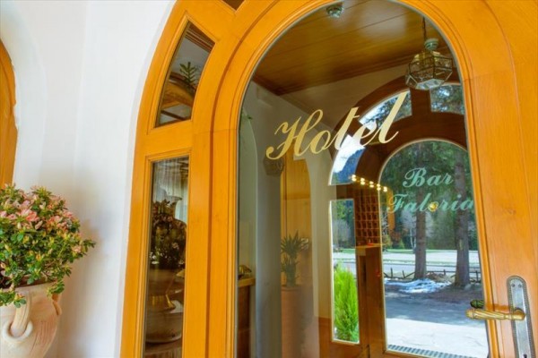 Sklenené dvere s nápismi „Hotel“ a „Bar Faloria“ vedúce do interiéru budovy s oblúkovitými dverami.