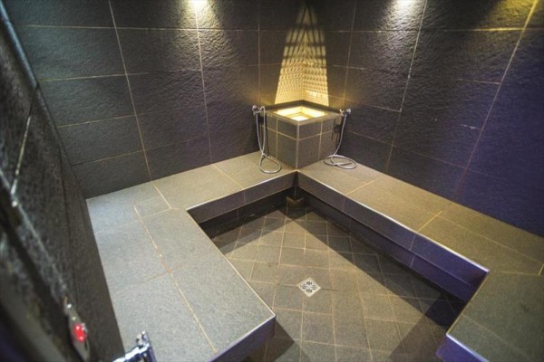 Parná sauna s tmavým obkladom a kamennými lavicami.