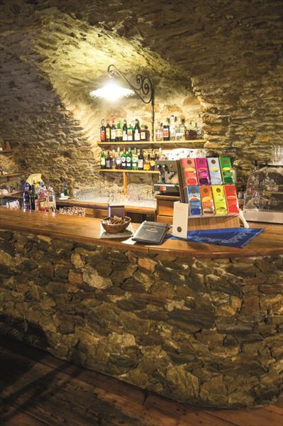 Kamenný bar s fľašami alkoholu a kávovarom v rustikálnej pivnici.  