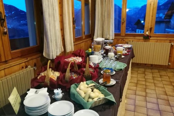 Bufetový stôl s jedlom a nápojmi pri okne s výhľadom na hory.