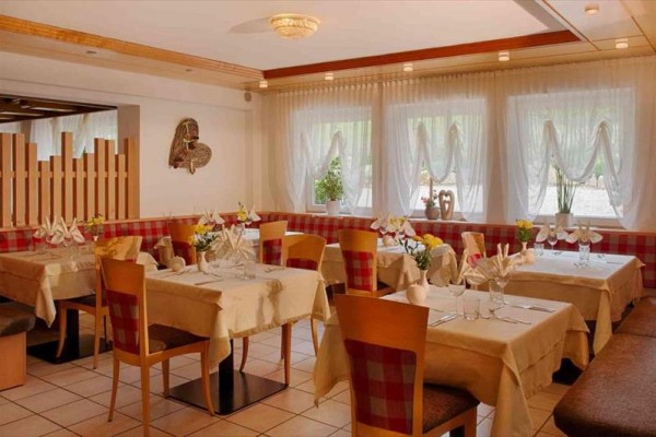 Elegantná reštaurácia s drevenými stoličkami a prestretými stolmi pri okne s kvetmi.
